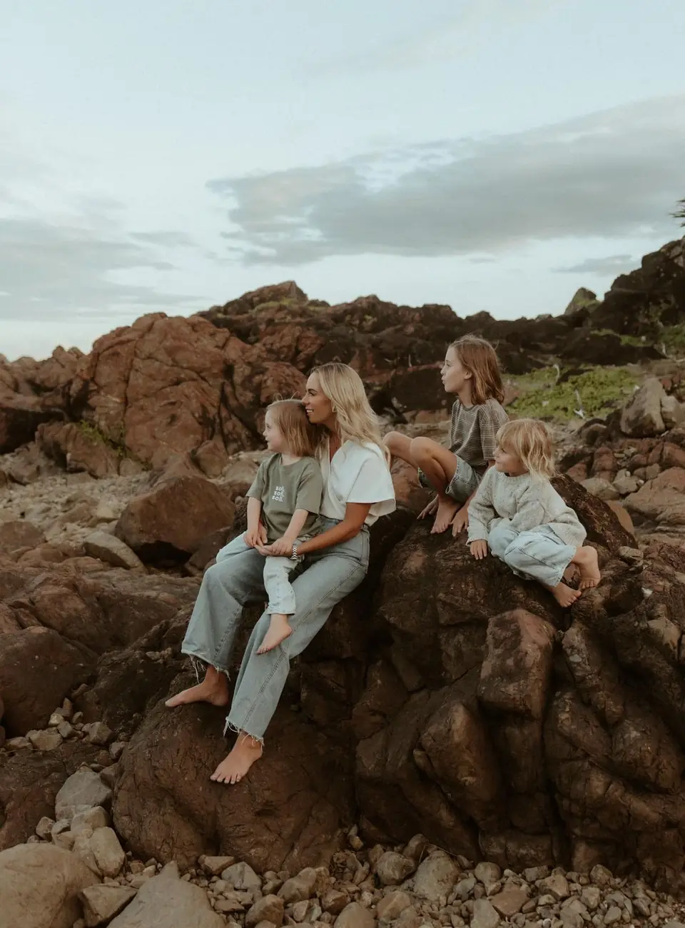 Ali Caley sitting on coastal rocks with her three children, looking out to sea